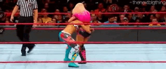 two female wrestlers are wrestling in a ring with a referee watching .