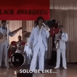 a man in a suit is singing into a microphone on a stage while a band plays behind him .