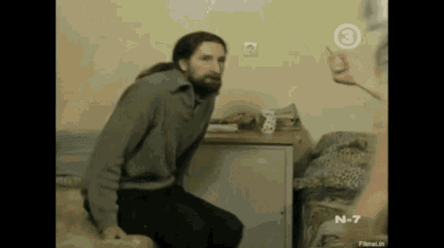 a man with long hair and a beard is sitting in a room with a number 3 on the wall
