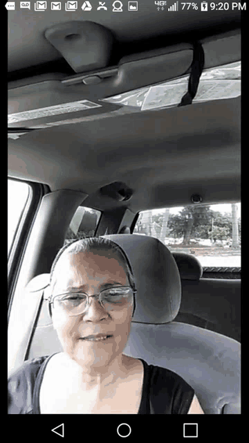 a woman wearing glasses is sitting in the back seat of a car with the time of 9:20 pm