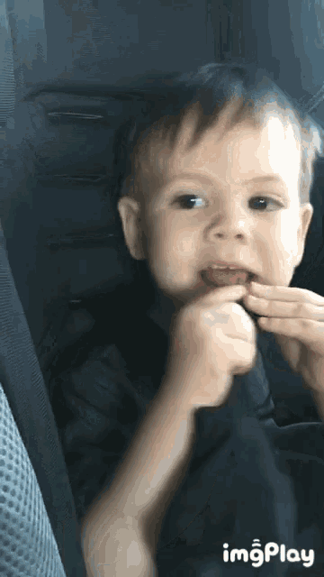a little boy is sitting in a car seat eating something