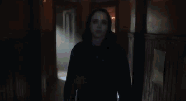 a woman in a black hoodie is standing in a dark hallway .