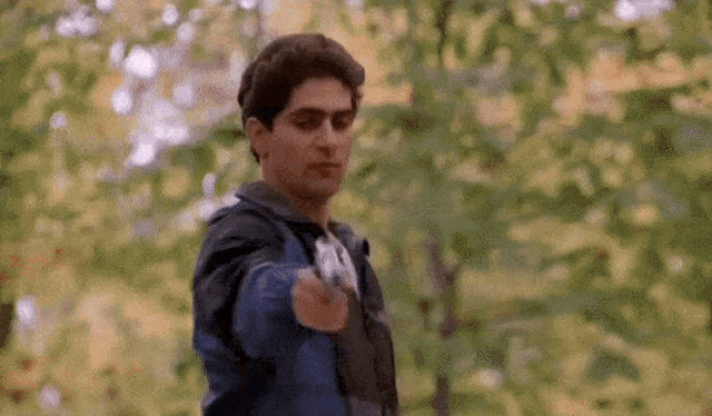 a man is pointing a gun at the camera while standing in the woods .