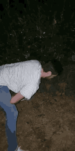 a man in a striped shirt is standing in the dirt with his head in the dirt .