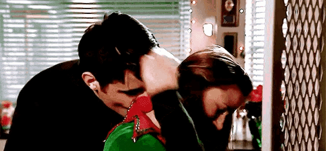 a man and a woman are kissing in a room with a christmas tree in the background .