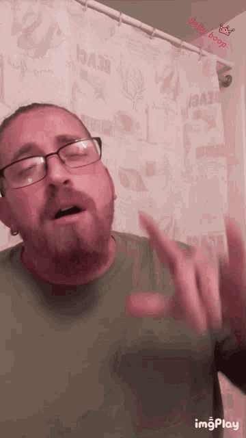 a man with glasses and a beard is standing in front of a shower curtain that says beach