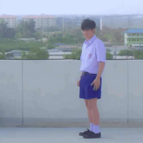 a young man in a white shirt and blue shorts is standing on a balcony