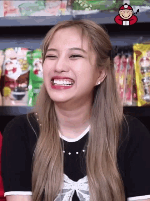 a woman with long blonde hair is smiling in front of a shelf of food