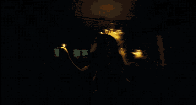 a woman in a dark room holding a candle in her hand