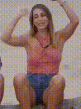 a woman in a pink top and blue shorts is sitting on a rock .