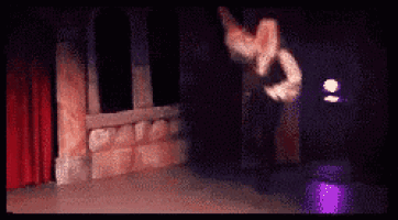 a man is dancing on a stage in a dark room with a red curtain .