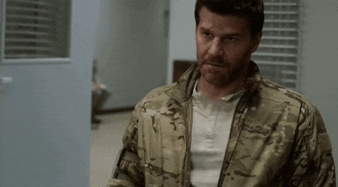 a man in a camouflage jacket is standing in a room and looking at the camera .