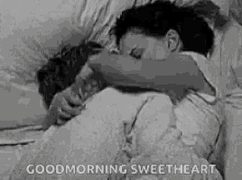 a black and white photo of a couple hugging each other in bed .