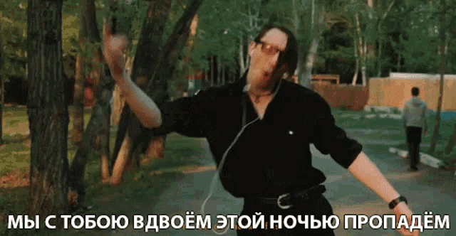a man in a black shirt and glasses is dancing in a park with a caption in russian