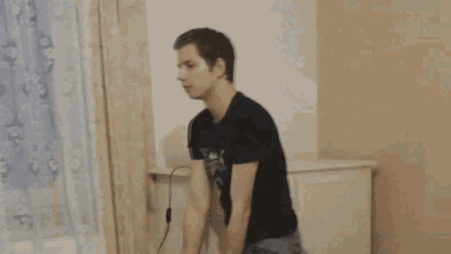 a young man wearing a black t-shirt with the word trick on it is standing in front of a white wall .
