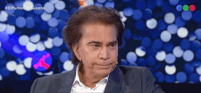 a man in a suit and white shirt is making a funny face in front of a blue background