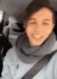 a woman wearing a scarf and a seat belt is sitting in a car and smiling .