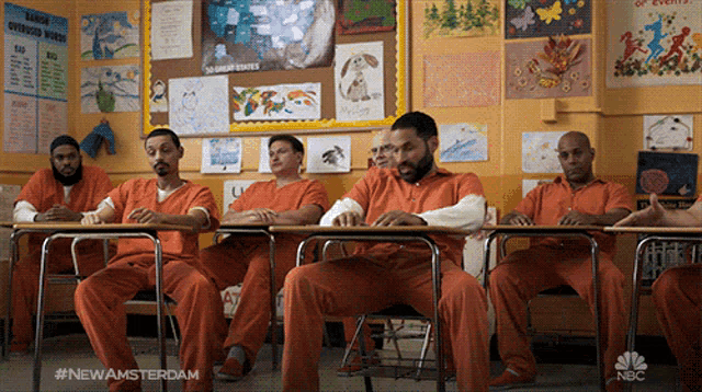a group of men in orange jumpsuits sit at desks in a classroom with the hashtag newamsterdam