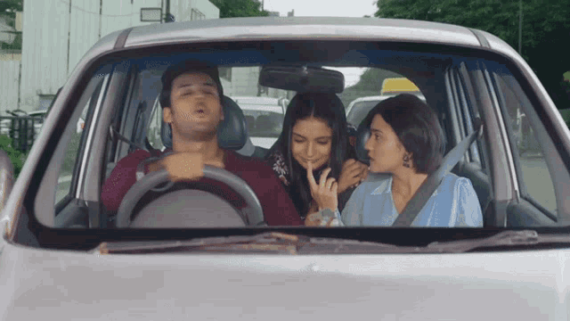 a man driving a car with two women sitting in the back seat