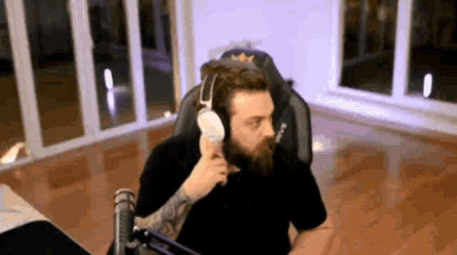 a man with a beard is wearing headphones and eating an ice cream cone while sitting in a chair .