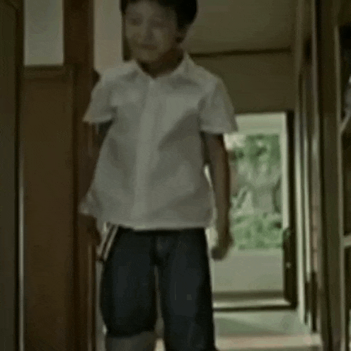 a young boy in a white shirt and blue shorts is standing in a hallway holding a book .