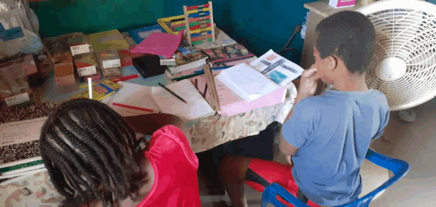 a boy and a girl are sitting at a table with a fan and books on it