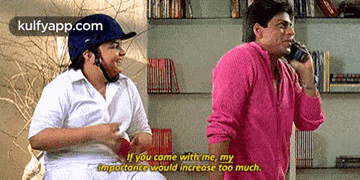 a man in a pink shirt is talking on a cell phone next to another man in a helmet .