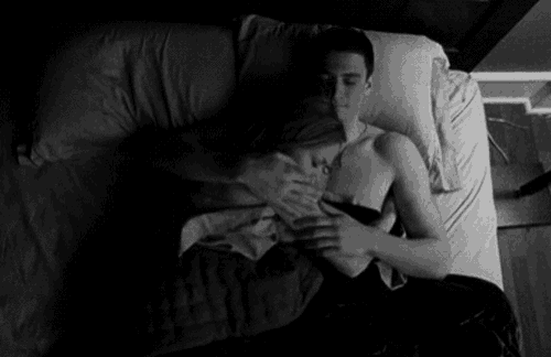 a man is holding a woman in his arms while laying in bed .