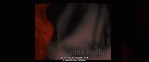 a woman in a red raincoat is talking into a microphone with the name john heard on the bottom
