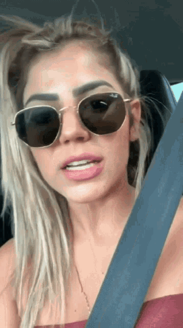 a woman wearing sunglasses is sitting in a car with her seat belt on