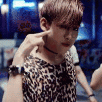 a young boy wearing a leopard print shirt and choker is pointing at his ear .