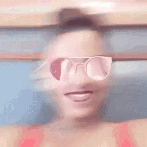 a woman wearing pink sunglasses and a red top is laughing .