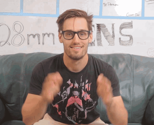 a man wearing glasses is sitting on a couch in front of a white board that says 28mm ns