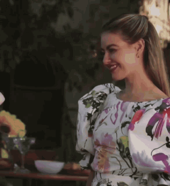 a woman in a floral dress smiles while standing next to a table