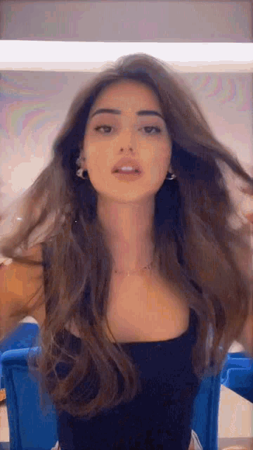 a woman with long hair is wearing a black top and earrings .