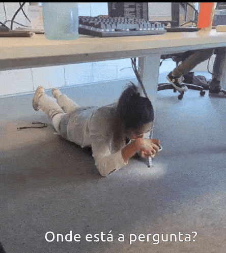 a woman laying on the floor under a desk with the words onde esta a pergunta
