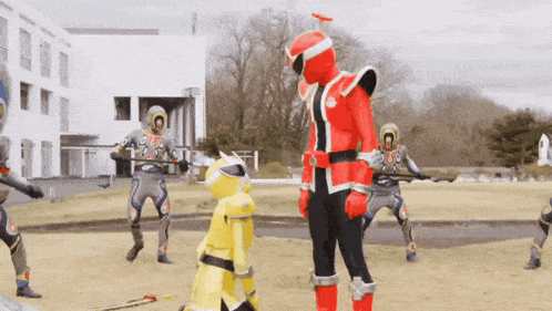 a group of superheros are standing in a field and one of them is wearing a red costume