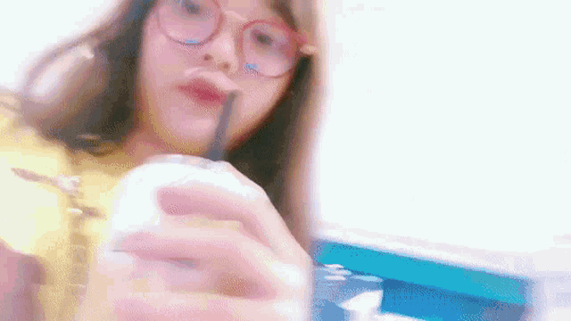 a woman wearing glasses and a yellow shirt is drinking from a cup with a straw .