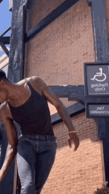 a man in a black tank top is standing in front of a handicap sign
