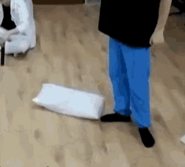 a man in blue pants is standing next to a pillow on the floor .