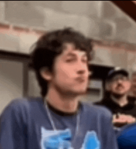 a man in a blue shirt is making a funny face while standing in a crowd .