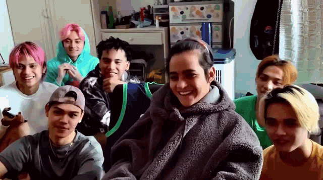 a group of young men are sitting in a room and one of them is wearing a gray coat