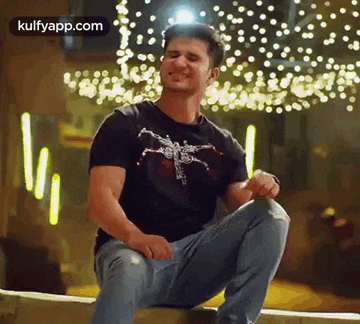 a man in a black t-shirt and jeans is sitting on a ledge .