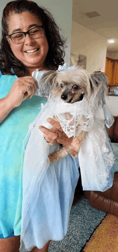 a woman is holding a small dog in a white dress