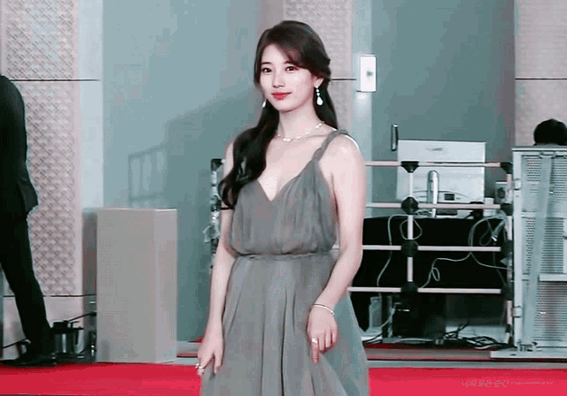 a woman in a grey dress is standing on a red carpet with a computer monitor in the background