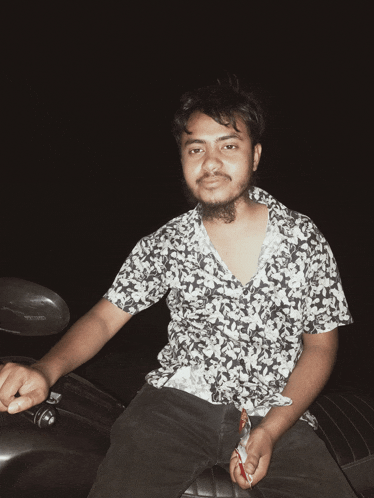 a man in a floral shirt is sitting on a motorcycle and smoking a cigarette
