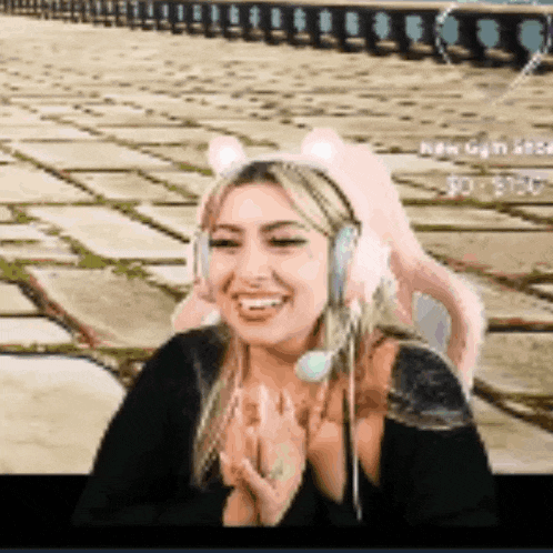 a woman wearing headphones and a cat ear headband is smiling and clapping .