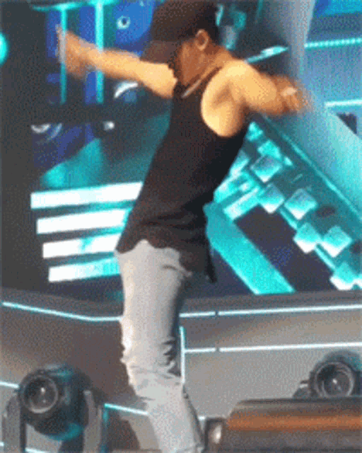 a man in a black tank top is dancing on a stage with his arms outstretched