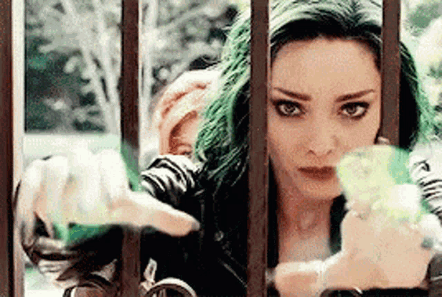 a woman with green hair is behind a fence holding a bottle .