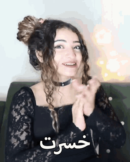 a woman wearing a black lace top is clapping her hands in front of a sign that says خسرت